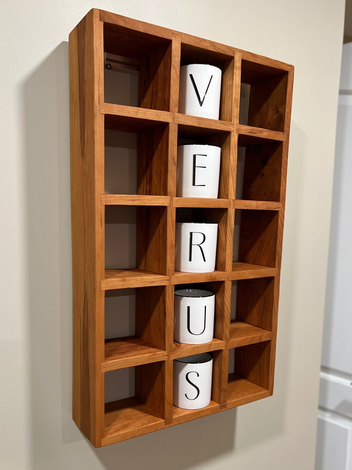 Wooden wall shelf with lettered mugs hanging on a neutral wall.