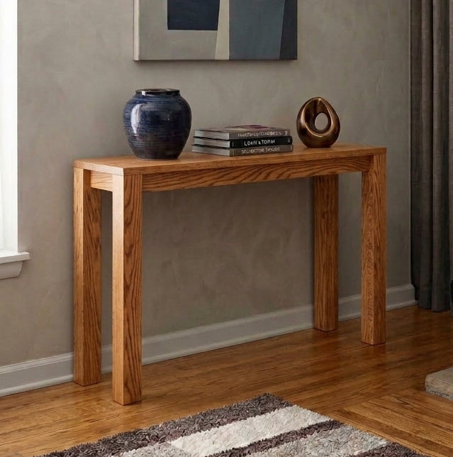 A modern living room scene featuring a light brown wooden console table against a textured beige wall, decorated with a blue ceramic vase and a small wooden sculpture. A large abstract geometric painting hangs on the wall.